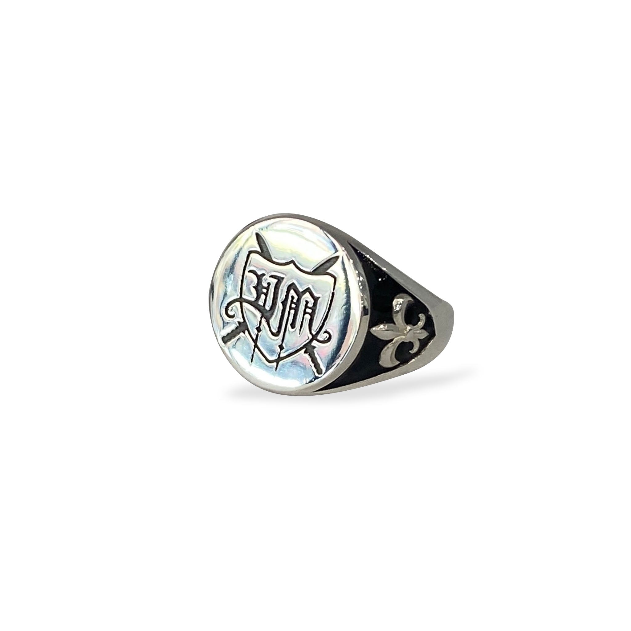 Sterling silver custom logo signet ring with engraved emblem on circular face, black enamel background, and fleur-de-lis shoulder detailing.