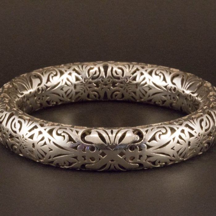 Sterling silver bangle with skull and crossbones design, intricate cut-out scrollwork pattern, polished wide circular band.