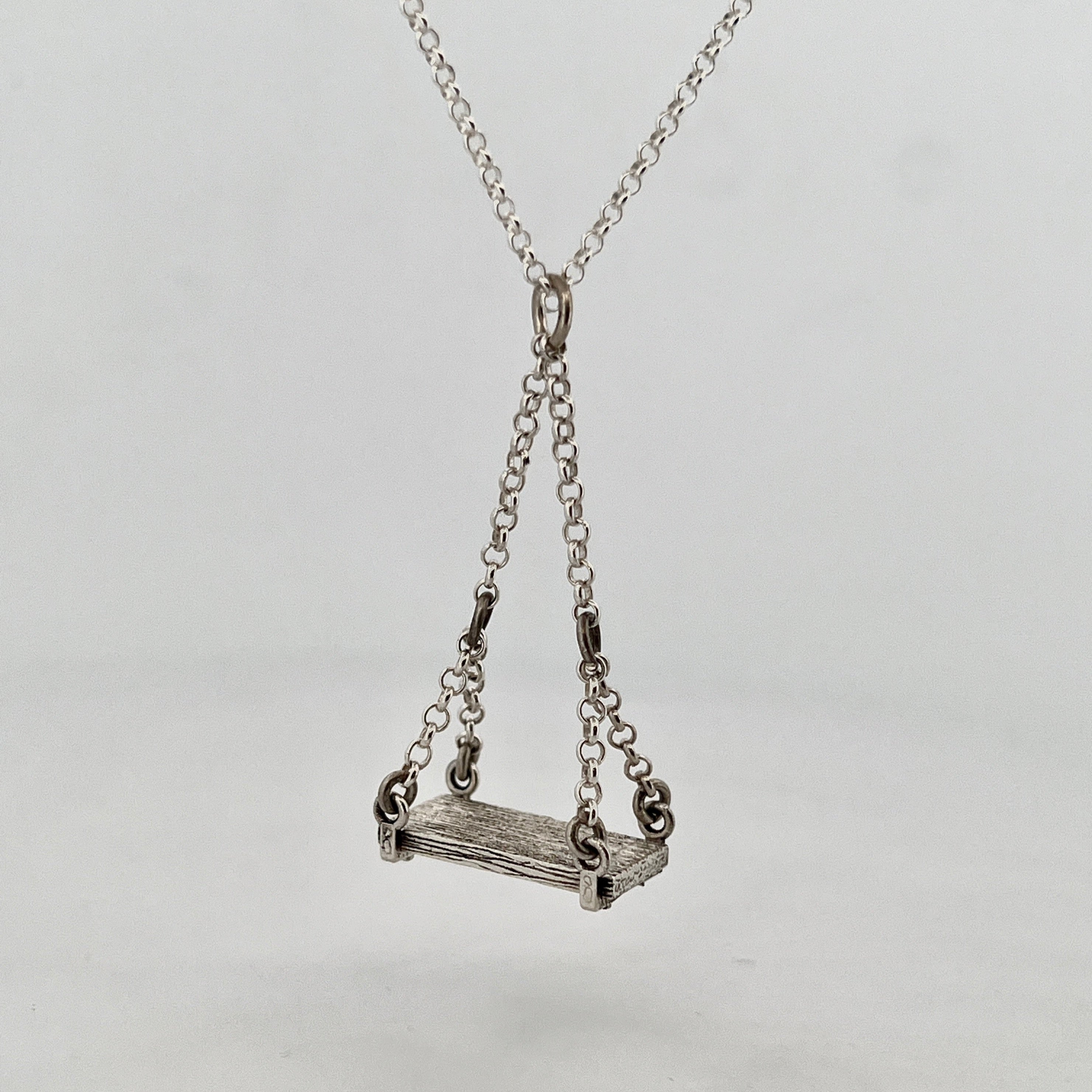 Sterling silver pendant necklace featuring a miniature swing with detailed wood grain texture and articulated chain links, handmade jewellery Newtown.