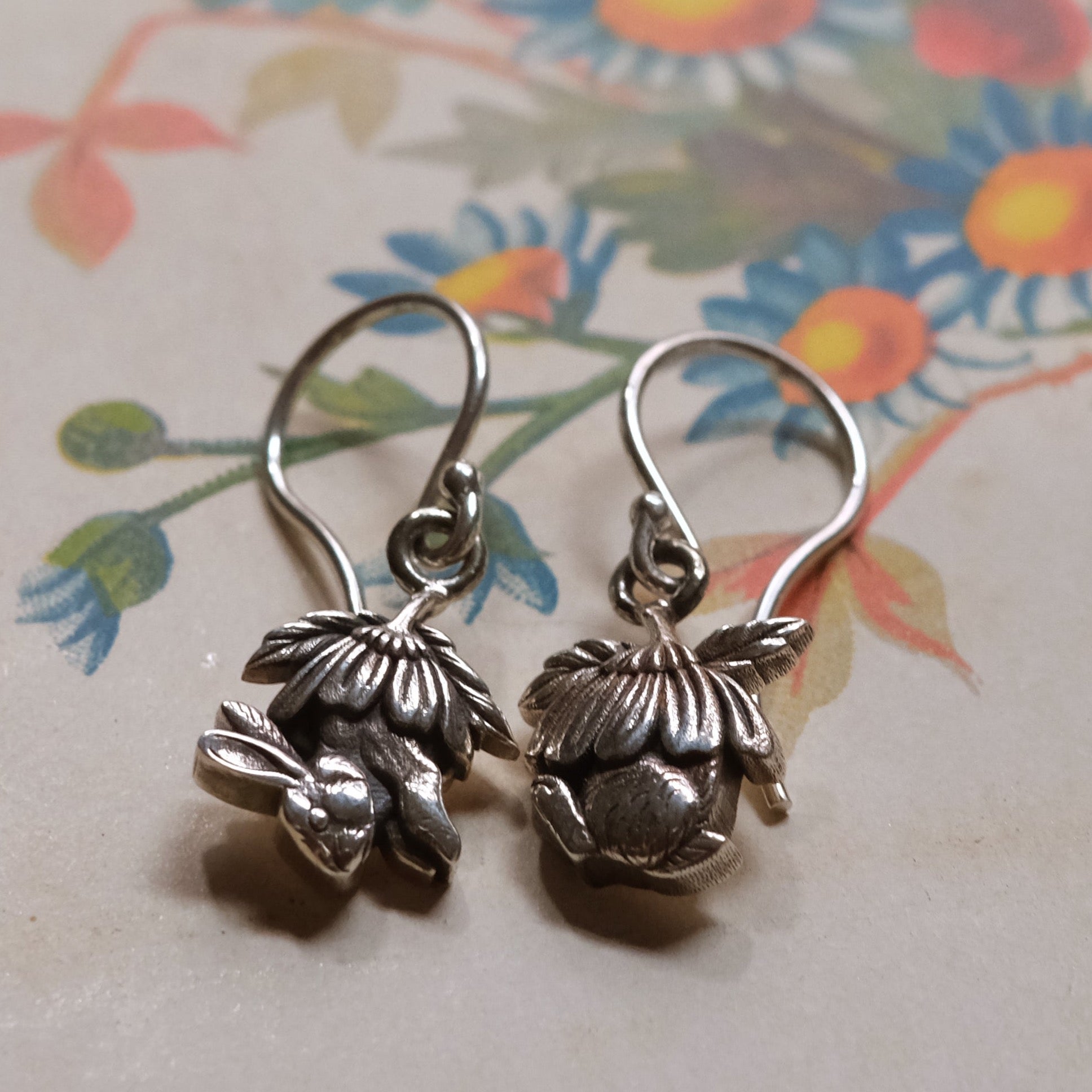 Sterling silver drop earrings with sculpted half bunny forms under layered daisy flower caps, handmade woodland jewellery