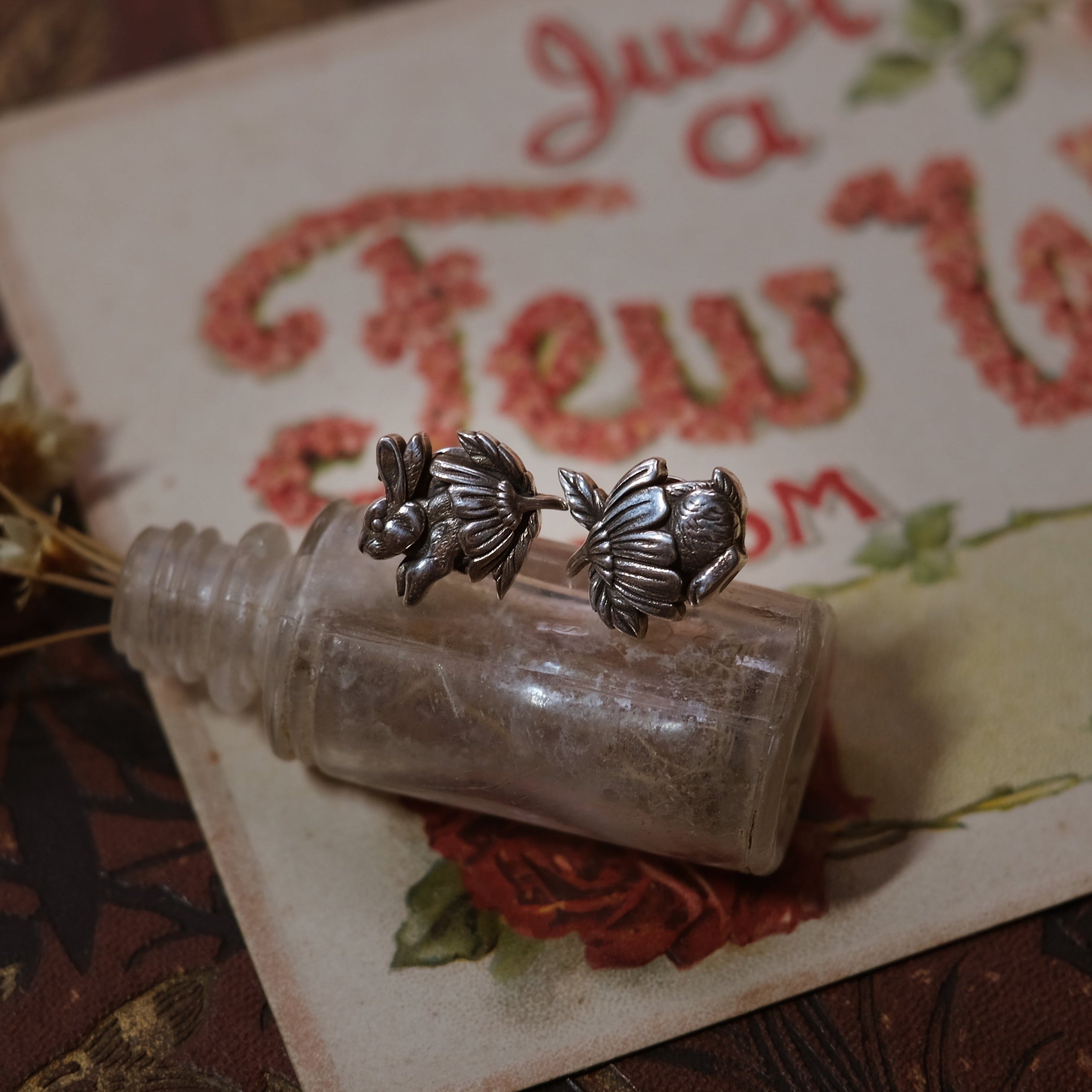 Sterling silver bunny stud earrings showing front and back half of bunny nestled in daisy flower caps, handmade whimsical design